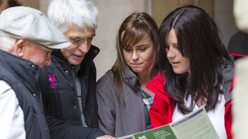 A  close-up of two house guides pointing out something in a pamphlet to two visitors
